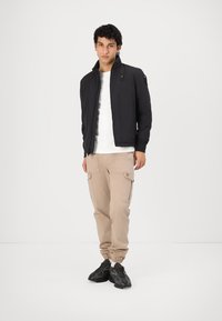 Black zip-up jacket with a stand collar, beige cargo pants with pockets, and black sneakers. Simple design, smooth texture, and functional accents.