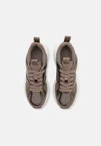 Barna sneaker, texturált panelek, világosbarna fűző, gumitalp és logó részlet a nyelvnél. A sima és mintás anyag kontrasztban áll egymással.