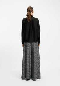 Blusa nera a maniche lunghe abbinata a una gonna maxi fluida, stampata in bianco e nero con un motivo a spina di pesce. Vista posteriore mostrata.