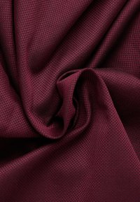 Bordeaux gekleurd textiel met een geweven patroon, dat een zachte, gladde afwerking en subtiele glans toont, in elegante plooien gedrapeerd.