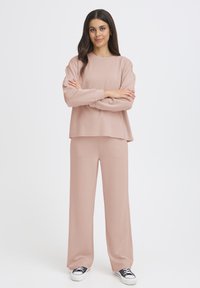 Hellrosa, locker sitzender Pullover und passende weite Hosen aus weichem Stoff. Verfügt über einen Rundhalsausschnitt und elastische Bündchen.