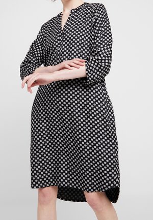 Vestido negro con cuello, mangas tres cuartos y un diseño estampado de puntos blancos. Presenta un dobladillo trasero ligeramente más largo.