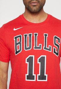 Červené bavlněné tričko s velkým černým nápisem "BULLS" a číslem "11" v texturovaném designu. Bílé logo Nike na levém rameni.