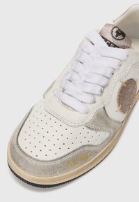 Sneaker in pelle bianca e suede grigio con design perforato, lacci bianchi piatti, etichetta con logo e suola in gomma beige. Accento dorato "ACBC".