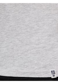 Nærbillede af lysegråt stof med en syet kant og et lille hvidt mærke med teksten "BIG STAR" og et stjerneikon nederst til højre.