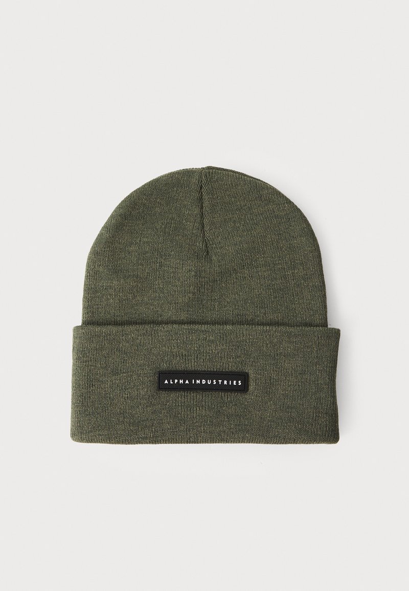 Olivově zelená pletená čepice s ohybem, s obdélníkovou černou etiketou s nápisem "ALPHA INDUSTRIES" v bílém textu. Měkká textura.