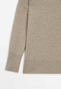 Manche de pull beige en maille tricotée et bas avec poignets et ceinture côtelés sur fond blanc.