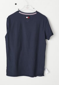 Camiseta de color azul marino con mangas cortas, cuello en V y rayas de color rojo y blanco en el cuello. Etiqueta visible en la parte posterior con el logo de la marca.