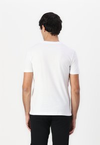 Camiseta blanca de manga corta, material de algodón, cuello redondo, silueta ajustada, textura suave. Diseño liso, sin patrones ni acentos visibles.