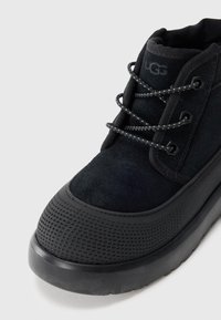Bottes noires avec une tige en daim, bout arrondi et semelle en caoutchouc texturé. Présente des lacets contrastants et un col rembourré pour le confort.
