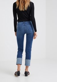 Blue denim jeans with a fitted design, featuring a cropped length and contrasting light blue frayed cuffs. Five pockets at the back.