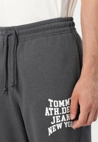 Grijze katoenen sweatpants met een elastische tailleband en trekkoord. Bevat witte bedrukte logotekst op het linkerpijp. Zachte stoftextuur.