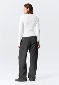 Haut blanc à manches longues côtelé avec une taille cintrée et des fentes latérales, associé à un pantalon ample gris foncé avec des poches arrière et une texture lisse.