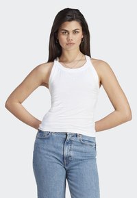 Haut sans manches blanc avec un col rond, fabriqué en tissu léger, présentant un petit logo. Assorti à un jean bleu taille haute.