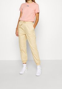Rosa kortärmad t-shirt med logotyp och rund halsringning, ihopparad med beige byxor med elastisk midja som har ankelfållar och sidofickor. Vita sneakers.
