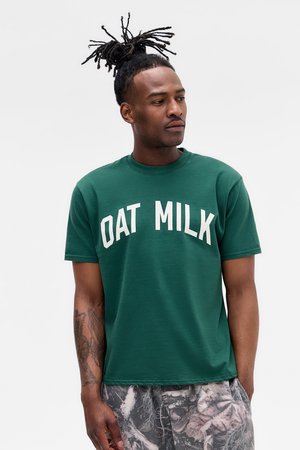 T-shirt vert à manches courtes avec le texte blanc "LAIT D'AVOINE". Design classique à col rond, fabriqué en tissu coton doux. Coupe décontractée.