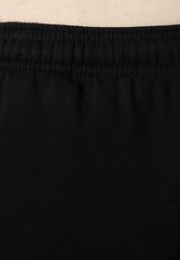 Tela de algodón negro con una textura suave, que presenta una cinturilla elástica fruncida y costuras bien definidas a lo largo del borde superior.