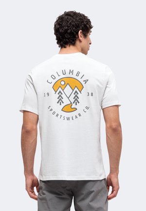 Mand iført hvid t-shirt med gult og sort Columbia Sportswear Co.-bjerglogo og tekst på ryggen.