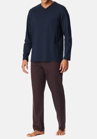 Marineblauses Langarmshirt mit V-Ausschnitt und Brusttasche, kombiniert mit gemusterten kastanienbraunen Hosen mit Rautenmuster und knöchellangem Schnitt.