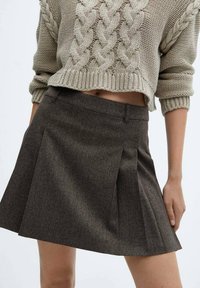 Brąskowa plisowana spódnica z fakturowanej tkaniny, z dopasowanym pasem i bocznymi kieszeniami, zestawiona z kremowym swetrem w splot warkoczowy.