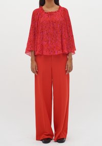 Blouse rouge plissée avec un motif floral, associée à un pantalon large rouge assorti. Tissu lisse avec une coupe décontractée et une texture douce.