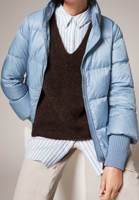 Light blue puffer jacket with a zip closure, brown knitted sweater underneath, and a striped blue and white shirt. Striped ribbed cuffs.