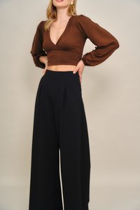 Braune, kurz geschnittene Bluse mit tiefem V-Ausschnitt und Puffärmeln, kombiniert mit hoch taillierter, weiter schwarzer Hose mit vorderen Falten.