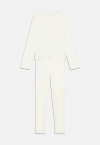 Langærmet hvid striktop og matchende bukser med rå kanter, lagt fladt på en hvid baggrund, bagfra.