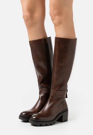 Bottes hautes jusqu'au genou en cuir marron avec une finition texturée, talons empilés et fermeture éclair. Présentent des lanières décoratives près de la cheville.