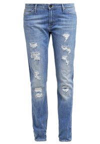 Jean en denim bleu clair avec une coupe slim, présentant des déchirures usées et des bords effilochés, cinq poches et une fermeture à boutons à la taille.