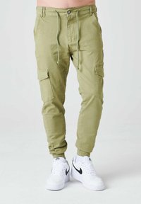 Pantalones cargo de color verde oliva claro con cintura con cordón, bolsillos inclinados y bolsillos laterales. Combinados con zapatillas Nike blancas.
