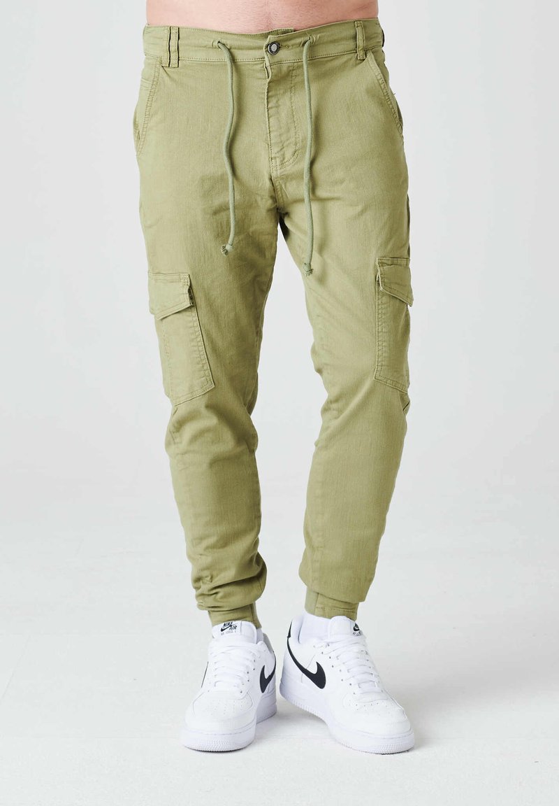 Pantalones cargo de color verde oliva claro con cintura con cordón, bolsillos inclinados y bolsillos laterales. Combinados con zapatillas Nike blancas.