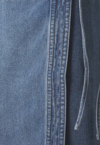 Ljusblå denimtyg med synliga sömmar och styg. En dragsko finns som framhäver den avslappnade designen.