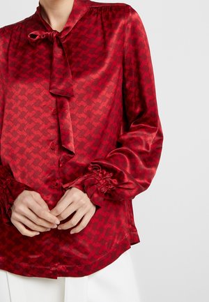 Rote Satinbluse mit dezentem Hahnentritt-Muster, langen Ärmeln, Knopfleiste, gebundenem Kragen und gerafften Manschetten für einen texturierten Effekt.