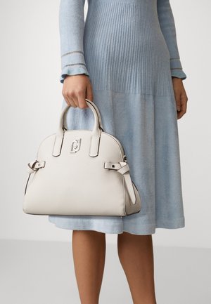 Femme portant une robe côtelée bleu clair tenant un sac à main blanc texturé avec des poignées arrondies et des détails de boucle.