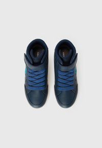 Een paar marineblauwe kindersneakers met blauwe veters en klittenbandsluitingen, vanuit bovenaf bekeken op een witte achtergrond.