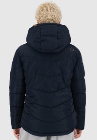 Giacca puffer blu navy con cappuccio, caratterizzata da un design a rombi e un accento in pelle marrone sulla spalla. Texture morbida e liscia.