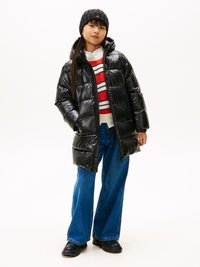 Giacca a vento nera con cappuccio e finitura lucida, abbinata a un maglione a righe rosse e bianche, jeans a gamba larga blu e stivali neri.