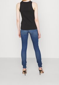 Canottiera nera a coste, jeans skinny blu e sandali con tacco alto. Concentrarsi sul design aderente e sulla texture del tessuto liscia.