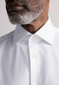 Weißes Hemd mit Button-Down-Kragen und strukturiertem Stoff, mit sichtbaren Knöpfen und Nahaufnahme des Kragenbereichs.