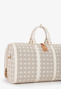 Borsa da viaggio realizzata in tessuto intrecciato color crema con motivo geometrico dorato, dotata di dettagli in pelle bianca, doppi manici e chiusura con zip.