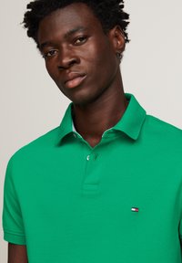 Groene polo shirt van textuurstof, met een knoopsluiting van drie knopen en een klein logo op de linkerborst. Met kraag en korte mouwen.