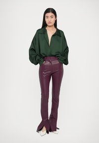 Bluza verde din satin cu decolteu adânc în V și mâneci supradimensionate, asortată cu pantaloni din piele bordo, cu croială strâmtă și tivuri despicate. Pantofi albi cu vârf ascuțit.