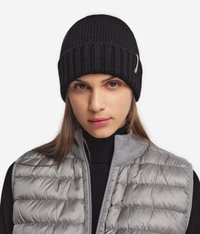 Svart ribbad stickad mössa med en tight passform. Bärs med en grå pufferväst med hög krage och quiltad textur.