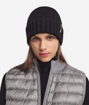 Zwarte geribde tricot beanie met een strakke pasvorm. Draagt een grijze puffervest met een hoge kraag en een gekatoen textuur.