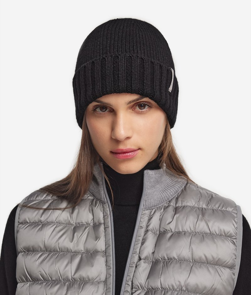 Svart ribbad stickad mössa med en tight passform. Bärs med en grå pufferväst med hög krage och quiltad textur.