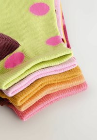 Pile de chaussettes en tricot pliées de couleur rose, orange, jaune et vert avec des pois roses sur une surface claire.