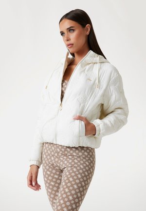 Giacca imbottita bianca con un design testurizzato, chiusura con zip e cappuccio, abbinata a leggings marroni con motivo. Presenta polsini e vita elasticizzati.