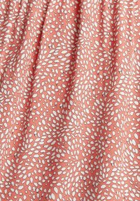 Korálová látka s nepravidelnými bílými a šedými rozptýlenými oválnými skvrnami, vytvářející texturovaný, vířící vzor.