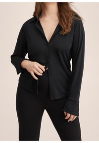 Camisa negra de botones hecha de una tela suave y elástica. Presenta mangas largas, un cuello clásico y un corte relajado.
